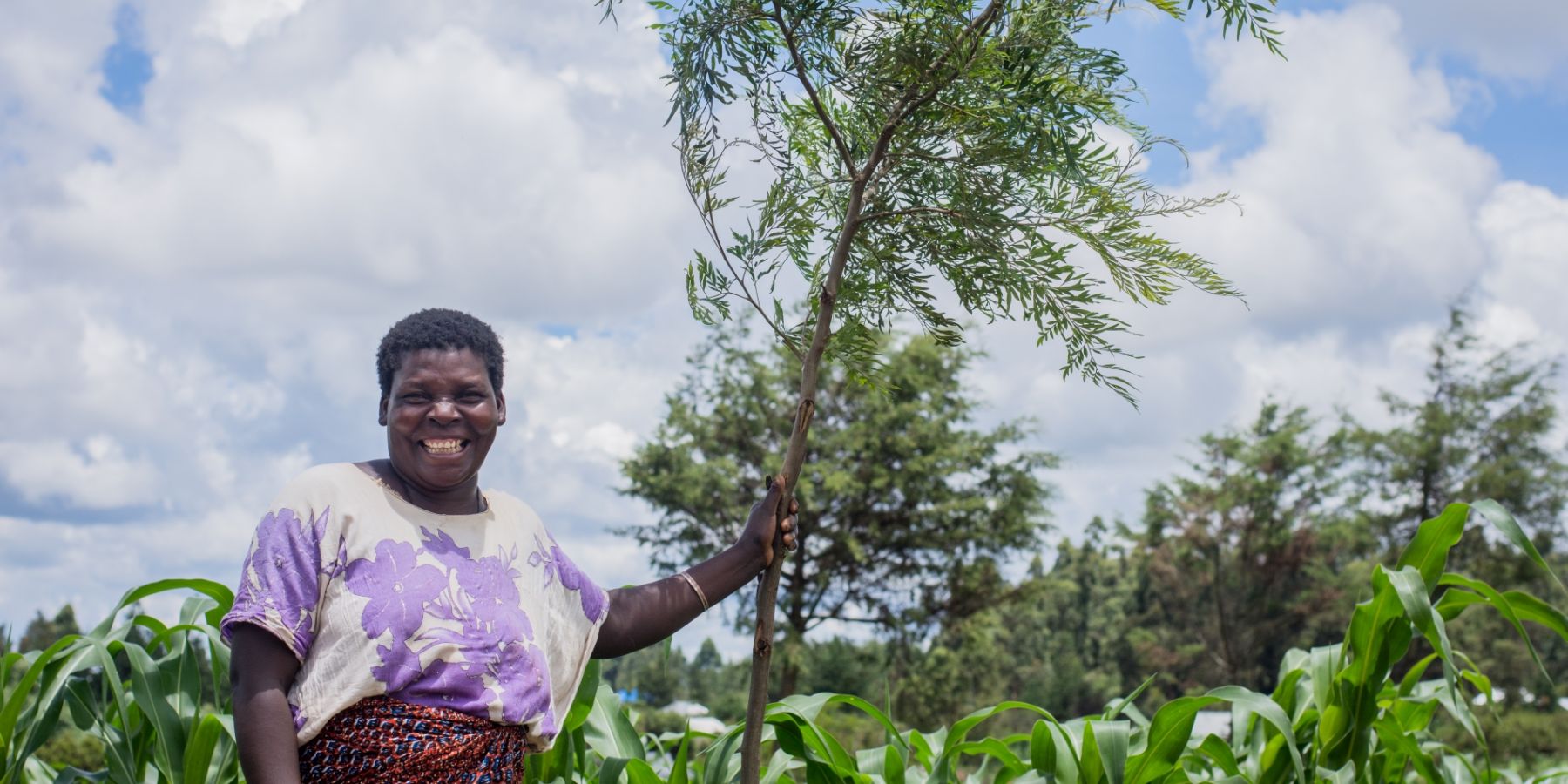 A farmer in Tanzania stands with her tree sapling