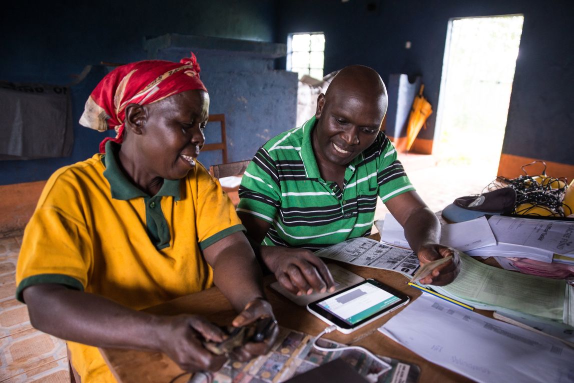 A Field Officer assists Difina Kimadi (left), one of the farmers we serve in Western Kenya, enrol for our program on a tablet.