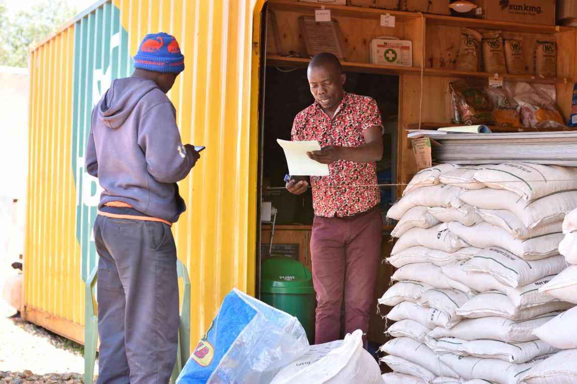 A farmer buys supplies for a shop housed in a yellow container