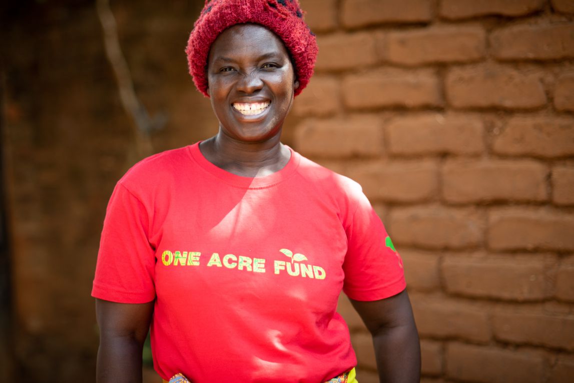 A smiling person wearing a red One Acre Fund t-shirt.  