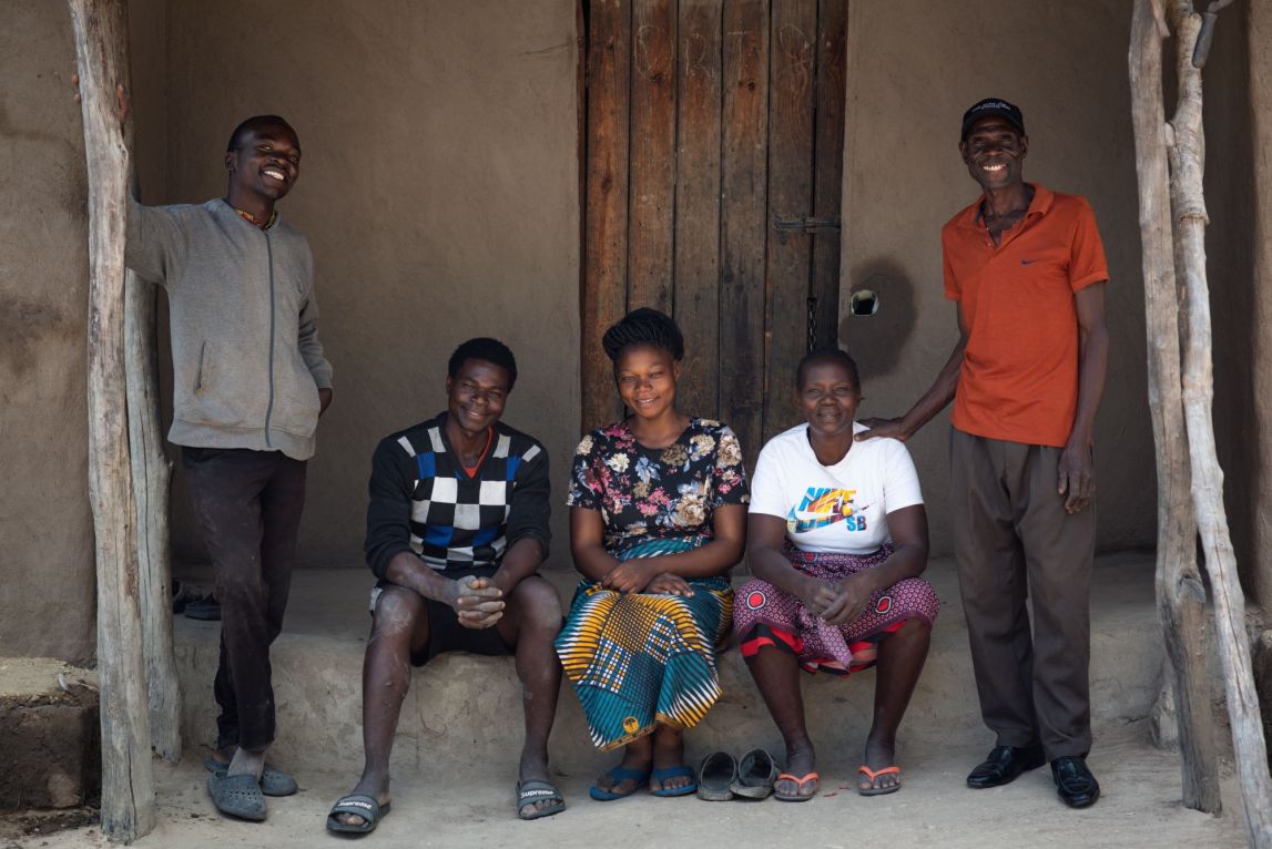 A smallholder farmer and his family sit in front of their home for a family portrait. 