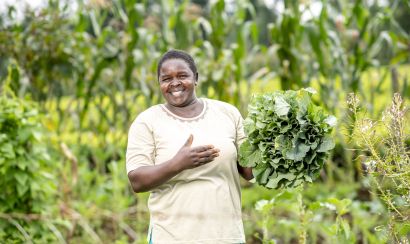 A farmer from Kapsabet, Kenya, stands holding a cabbage she's just harvested