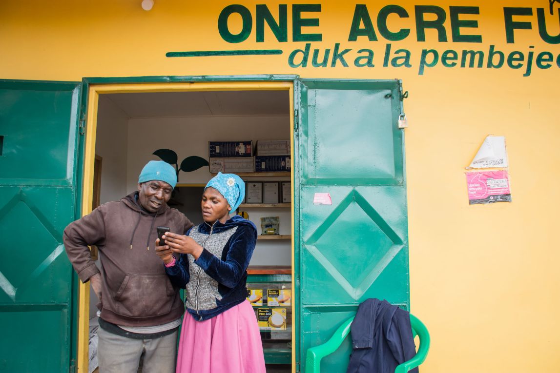 A One Acre Fund duka manager helps a customer outside a duka in Tanzania